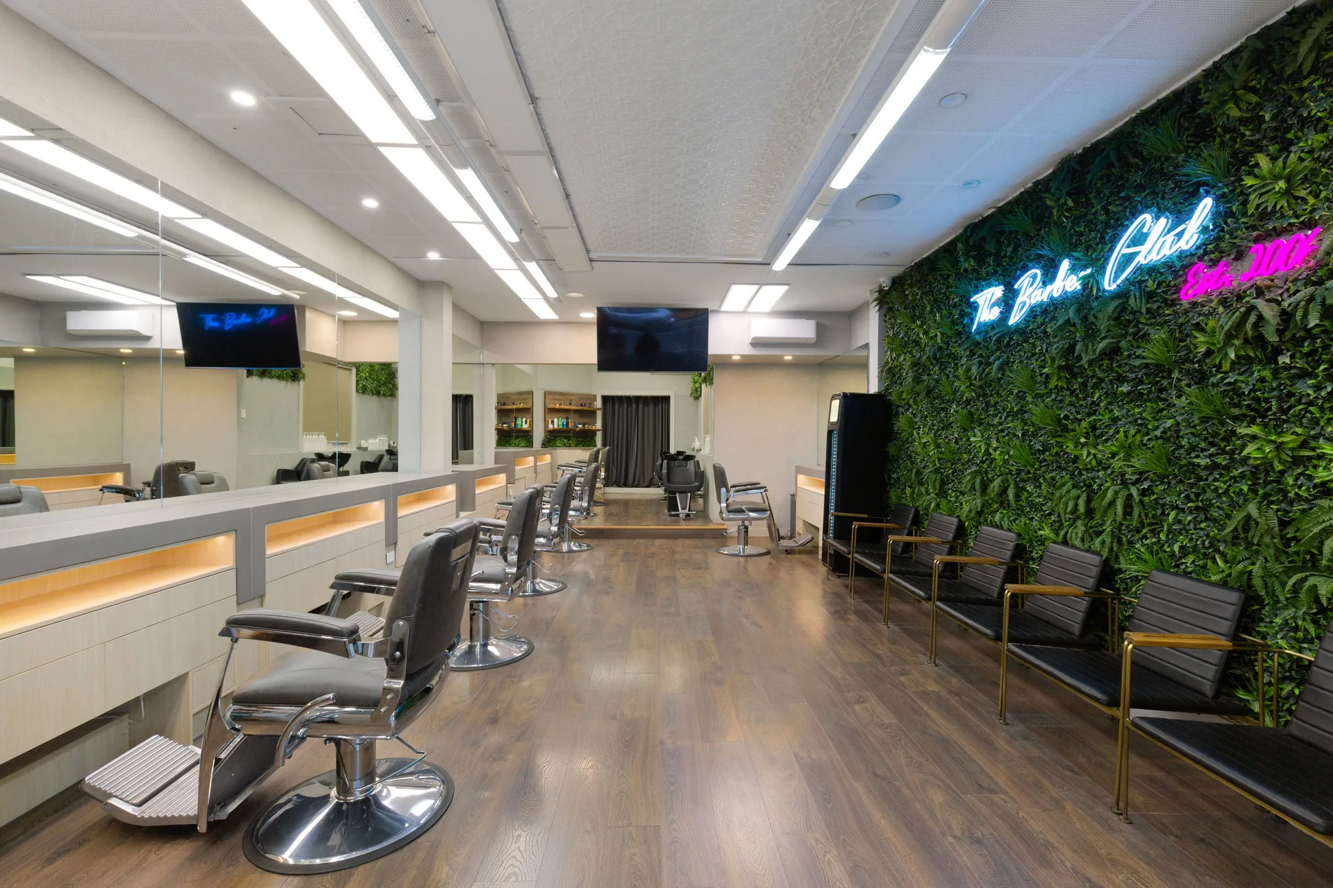 Inside The Barber Club Bentleigh at 375 Centre Rd, looking down the row of chairs to the green wall and Est. 2006 neon